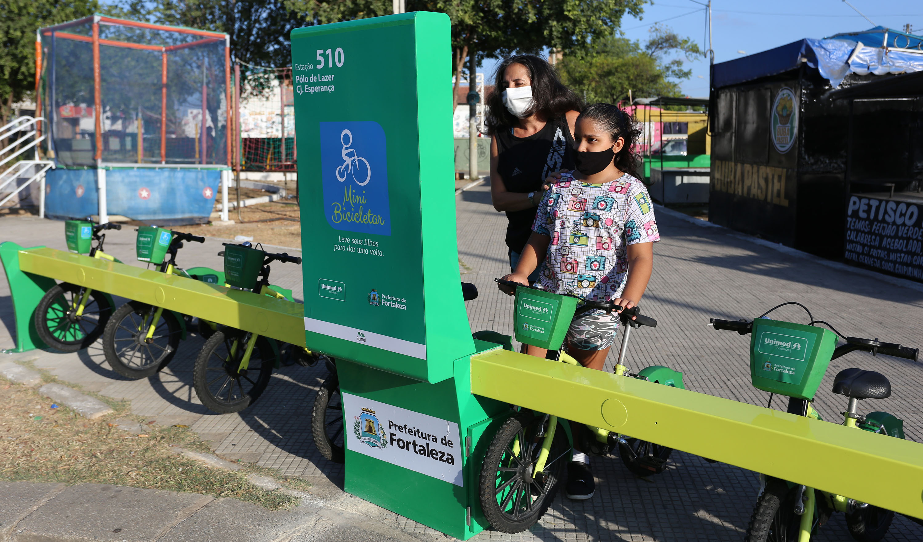 uma criança pega uma bicicleta na estação do mini bicicletar enquanto é observada pela mãe